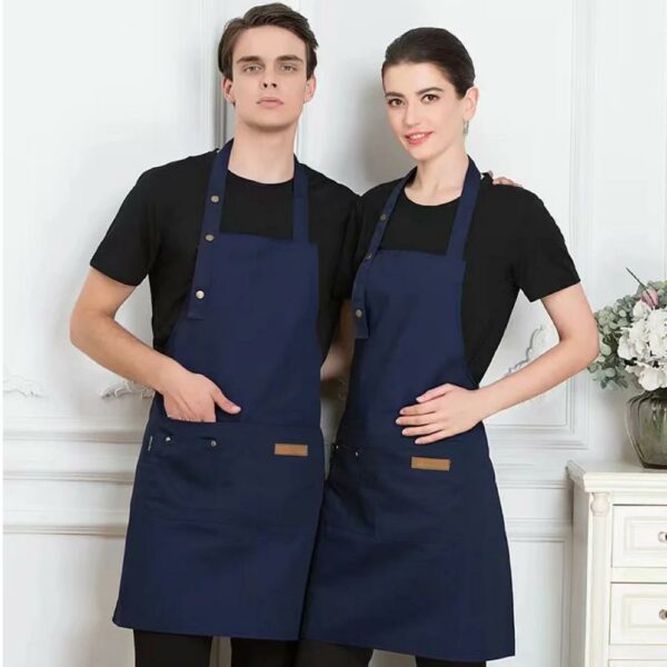 un homme et une femme dans la trentaine, portant un t-shirt noir avec un tablier de cuisine réglable bleu debout devant un mur blanc