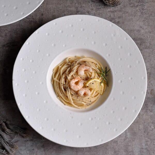 Assiette pates chic sobre, disposée sur une table grise avec des aliments à l’intérieur de l'assiette.